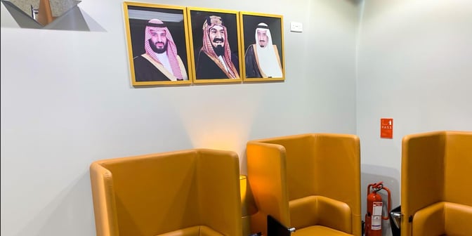 The seating area in Hayyak Lounge at Turaif Domestic Airport features high-backed chairs and wall-mounted portraits, providing a comfortable waiting space.