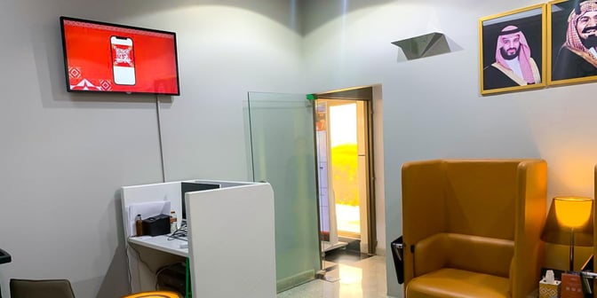 The Hayyak Lounge at Turaif Domestic Airport features a seating area with high-backed chairs, a TV, and a small workspace.