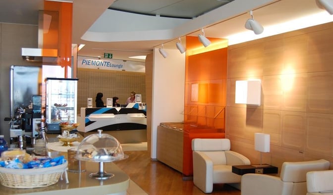 The Piemonte Lounge at Turin-Caselle Airport features a reception desk, seating area, and a self-serve snack station with beverages.