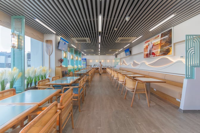 The SH Premium Lounge at Tuy Hoa Airport features a spacious seating area with tables, chairs, and a self-serve food station.