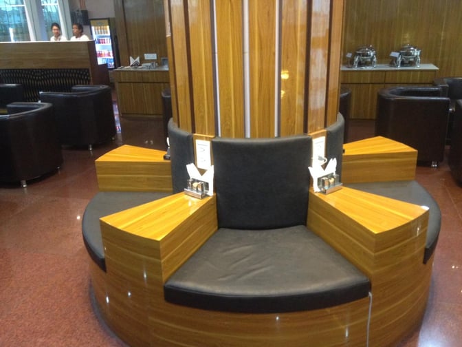 Circular seating in Vadodara Airport's Premium Lounge features integrated tables and nearby buffet stations for passenger convenience.