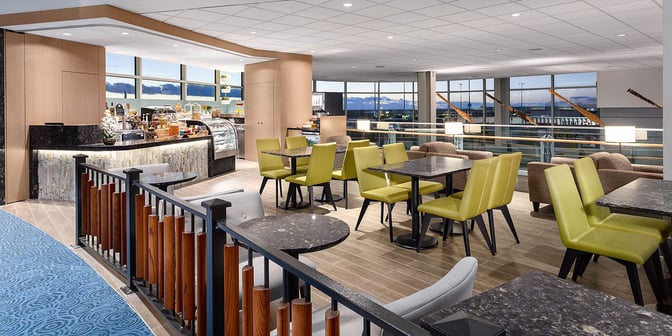The Plaza Premium Lounge, Domestic Gate C29 at Vancouver International Airport features a seating area with tables and chairs adjacent to a self-serve food counter.