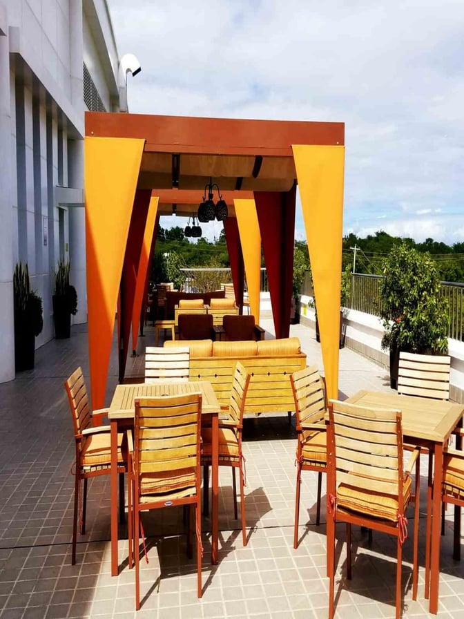 The outdoor seating area at V. C. Bird International Airport's Executive Lounge features tables and chairs under a covered patio.