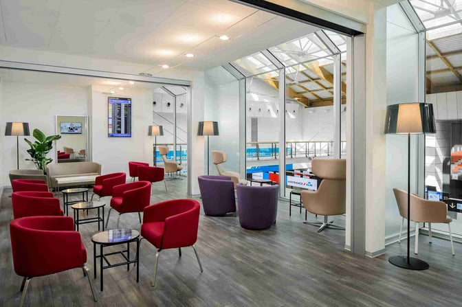 The Aspire Executive Lounge at Venice Marco Polo Airport features a seating area with armchairs, small tables, and a flight information screen.