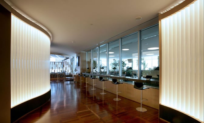 The Marco Polo Club lounge at Venice Airport features a corridor with bar-style seating and workstations along a glass wall.