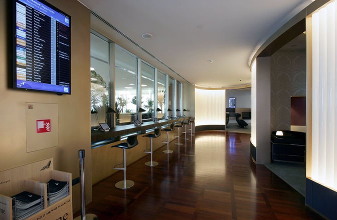 The Marco Polo Club lounge at Venice Airport features a counter with barstool seating and individual workstations equipped with tablets.