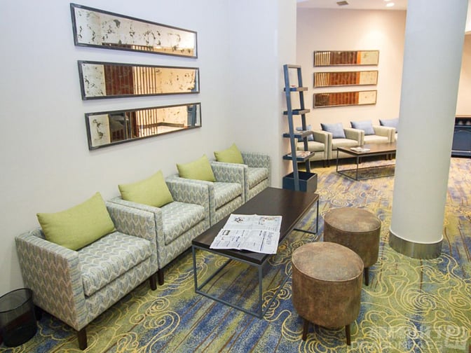 The seating area in Makuwa Lounge at Victoria Falls Airport features cushioned chairs, a coffee table with newspapers, and decorative wall mirrors.