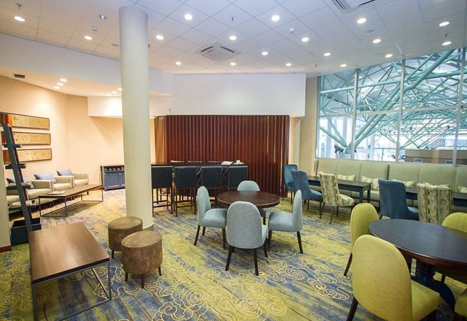 The Makuwa Lounge at Victoria Falls Airport features diverse seating options, including tables and chairs, with views of the terminal.