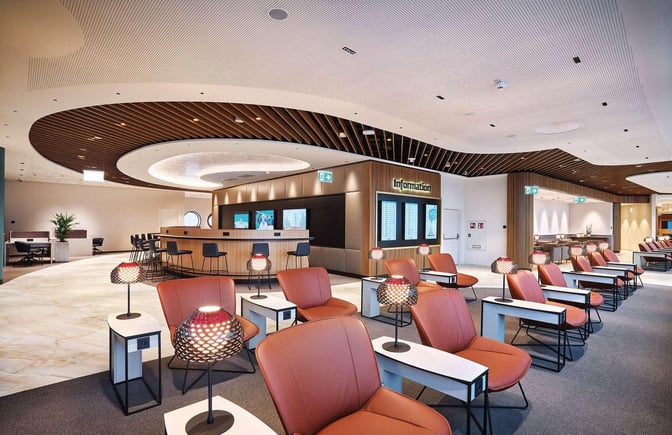 Seating area in Vienna Lounge at Vienna International Airport features comfortable chairs, individual tables with lamps, and an information desk nearby.