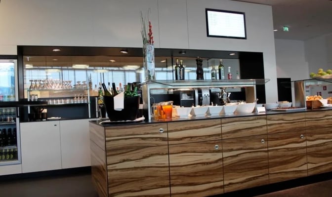 The Sky Lounge at Vienna International Airport features a self-serve food station with beverages, snacks, and a display of condiments.