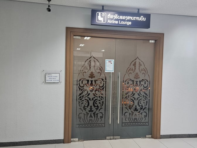 The entrance to the Airline Lounge at Wattay International Airport features decorative glass doors and a sign indicating daily operating hours.