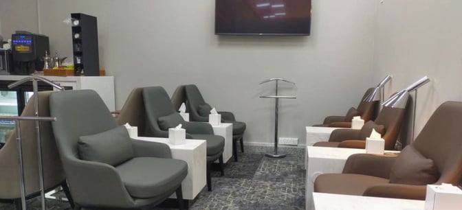 The seating area in Hayyak Lounge at Wadi al-Dawasir Airport features comfortable chairs with side tables and a television.