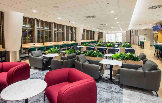 The Etiuda Executive Lounge at Warsaw Chopin Airport features a seating area with armchairs, tables, and integrated greenery for relaxation.