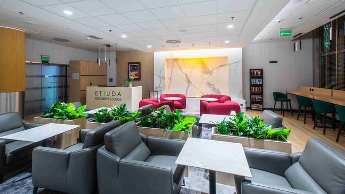 The Etiuda Executive Lounge at Warsaw Chopin Airport features comfortable seating with tables, greenery, and a reception area for guests.