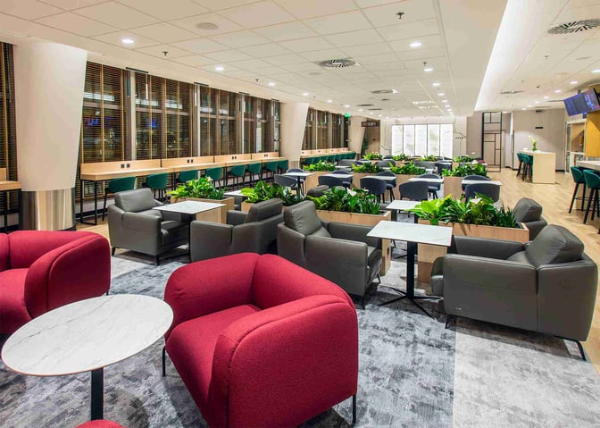 The Etiuda Executive Lounge at Warsaw Chopin Airport features a seating area with armchairs, tables, and a row of workstations.