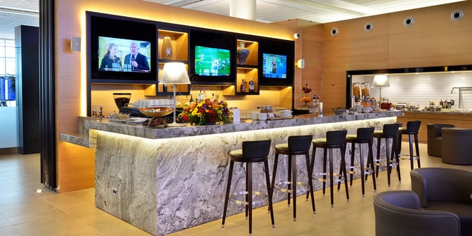 The bar at Plaza Premium Lounge in Winnipeg Airport offers a selection of beverages with counter seating and multiple televisions.