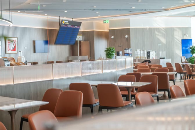 The seating area in China Eastern Lounge at Xi'an Xianyang International Airport features tables and chairs with a view of a flight information screen.