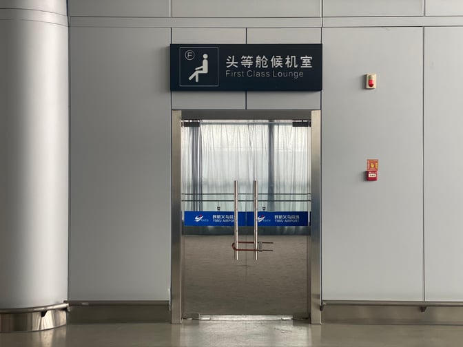The entrance to the First Class Lounge at Yiwu Airport features a glass door and clear signage above.