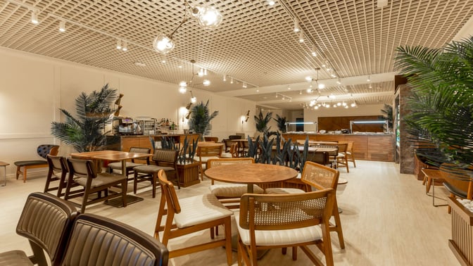 The Primeclass Lounge at Zagreb Airport features a seating area with tables and chairs, adjacent to a self-serve food station.