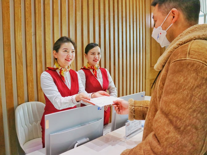 The reception desk at Zhangjiajie Hehua Airport's No. 4 First Class Lounge features staff assisting a guest with check-in procedures.
