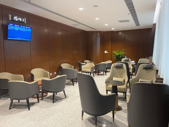 The seating area in Zhangjiakou Ningyuan Airport's First/Business Class Lounge features comfortable chairs and small tables, with a flight information display.