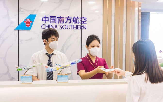 The reception desk at China Southern Lounge in Zhuhai Jinwan Airport features staff assisting a guest with check-in procedures.