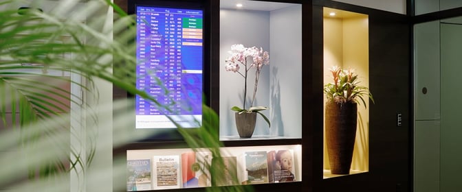The Aspire Lounge at Zurich Airport features a flight information screen, decorative plants, and a selection of magazines for guests.