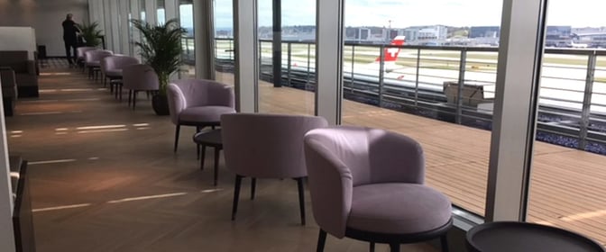Seating area in the Aspire Lounge at Zurich Airport offers comfortable chairs with views of the runway through large windows.